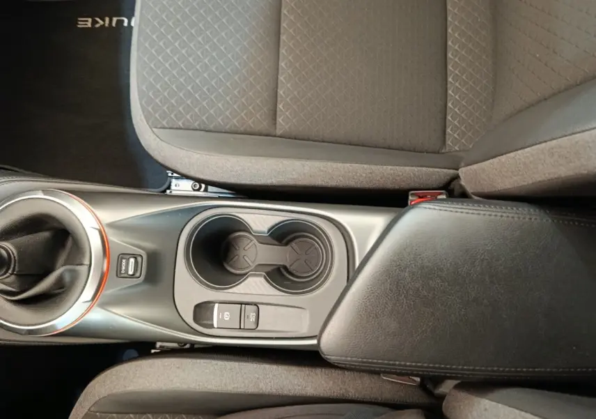 Vue plongeante sur la console centrale noire avec boîte manuelle et accoudoir entre les sièges gris du Nissan Juke 2025.