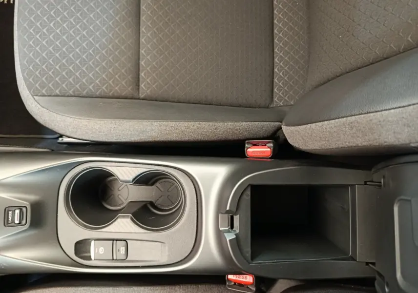 Vue plongeante sur la console centrale noire du Nissan Juke gris clair, avec porte-gobelets et accoudoir ouvert.