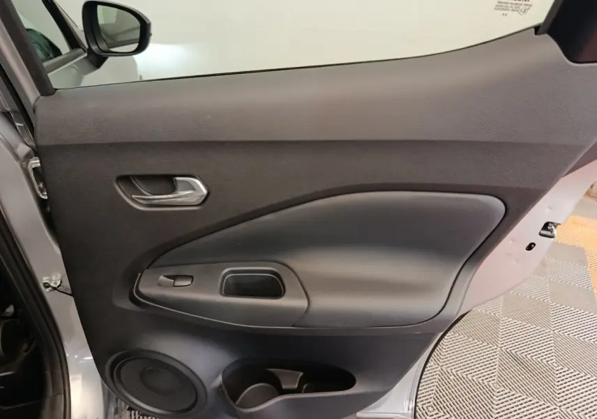 Vue intérieure côté gauche de la porte avant gris clair du Nissan Juke 2025 avec poignée et haut-parleur intégrés.