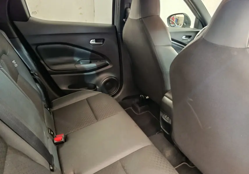 Vue intérieure arrière côté gauche du Nissan Juke 2025, sièges tissu gris foncé avec ceintures visibles.