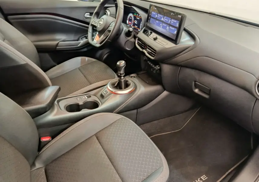 Vue intérieure côté passager du Nissan Juke 2025, montrant la console centrale avec levier de vitesse manuel et écran tactile.