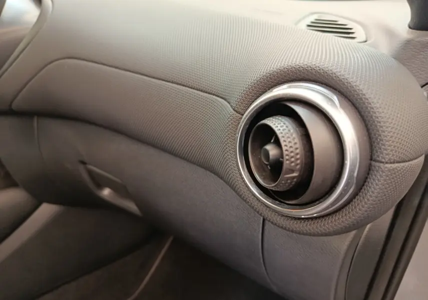 Détail de la sortie d'air ronde chromée côté passager du tableau de bord gris foncé du Nissan Juke 2025.