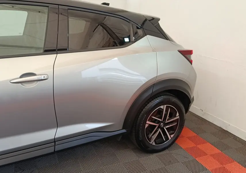 Vue latérale côté droit du Nissan Juke gris clair, mettant en valeur la roue arrière et la ligne de caisse dynamique.