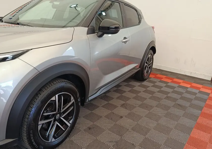 Vue 3/4 avant droit du Nissan Juke gris clair, soulignant ses jantes noires et détails de carrosserie lisse.