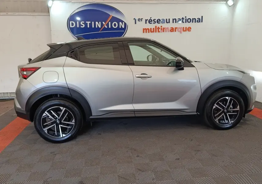 Nissan Juke gris clair vue de profil côté gauche, avec toit noir et jantes alliage noires en intérieur showroom.