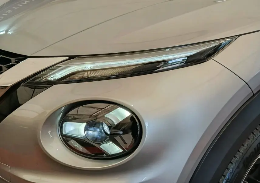 Gros plan sur le phare avant droit gris clair du Nissan Juke 2025 avec éclairage LED et partie de la calandre visible.
