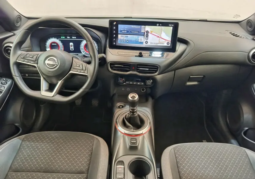 Vue intérieure avant du Nissan Juke DIG-T 114 BVM6 Acenta 2025, tableau de bord noir avec écran tactile et levier de vitesse manuel.