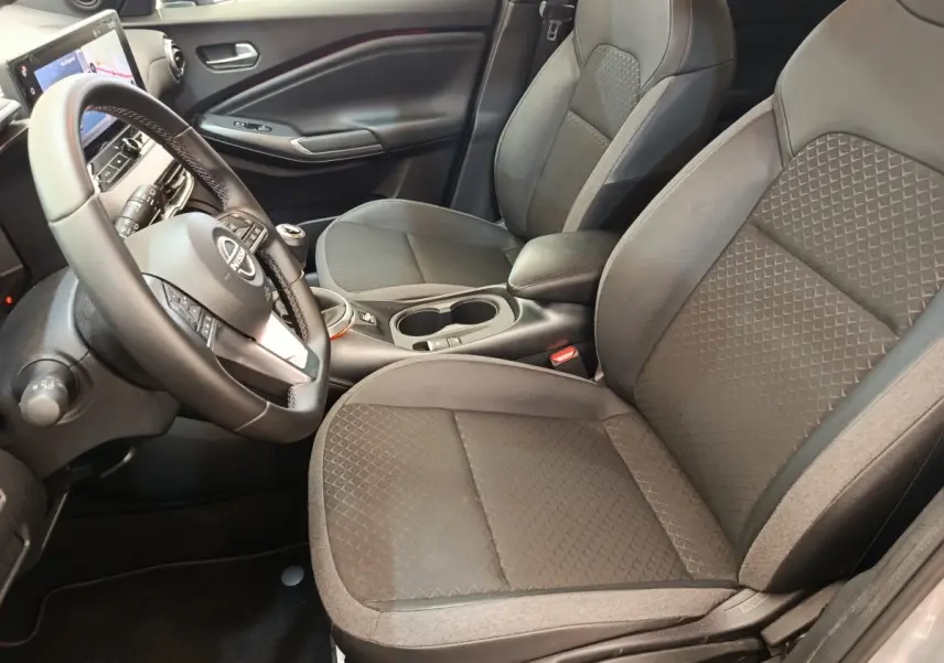 Vue intérieure avant droite du Nissan Juke 2025 gris clair, avec volant multifonctions et sièges tissu gris à motifs géométriques.