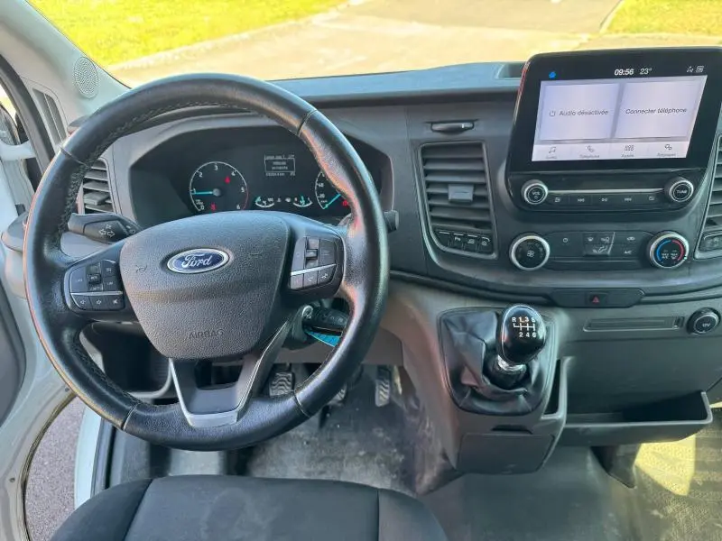 Vue intérieure du poste de conduite du Ford Transit Fourgon blanc, avec volant multifonction et levier de vitesses manuel visible.