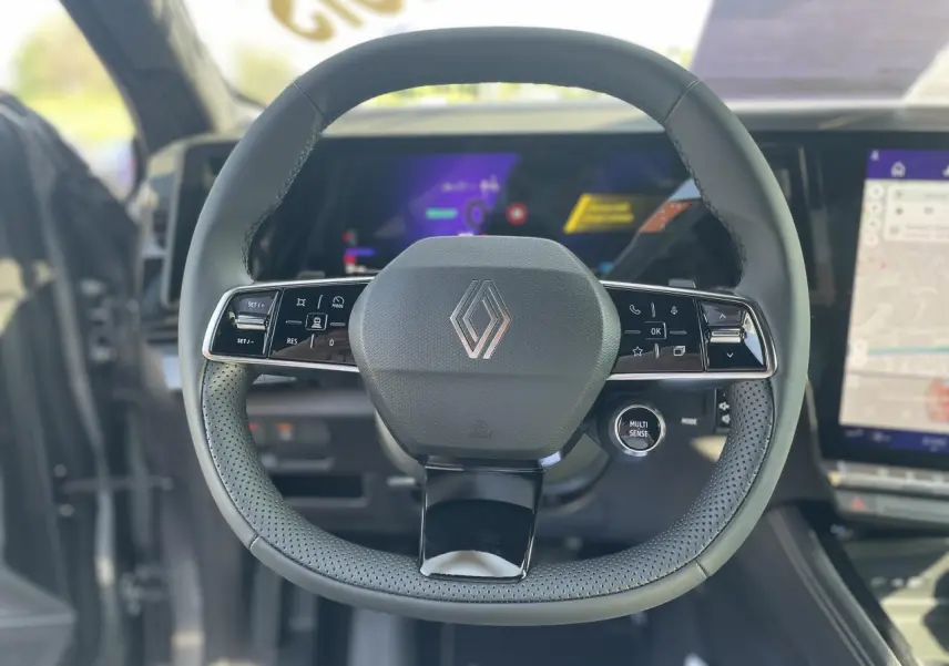 Volant Renault RAFALE 2025 en textile refined avec commandes intégrées, cadrans numériques et écran tactile visible en arrière-plan.