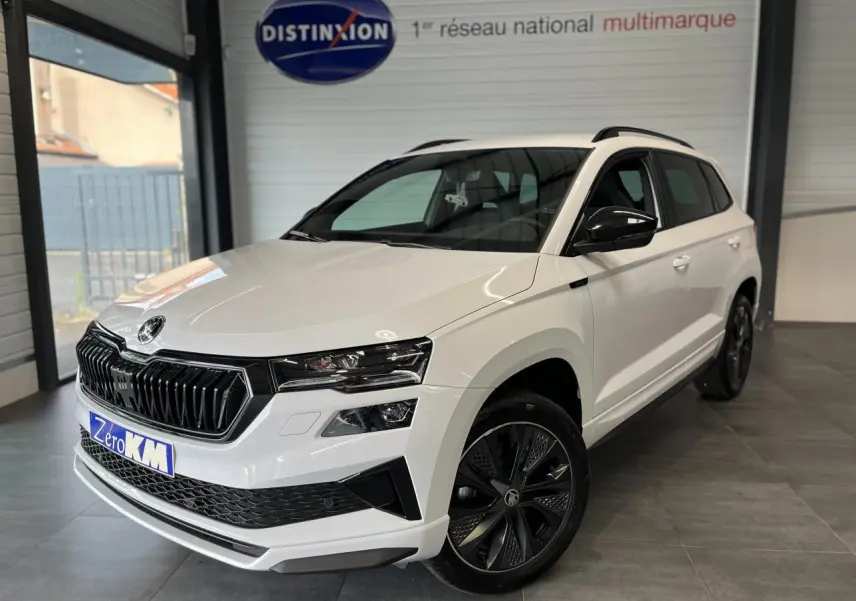 Vue 3/4 avant droite du SUV Skoda Karoq blanc avec calandre noire et jantes alliage anthracite en intérieur showroom.
