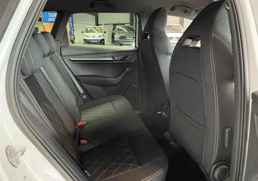 Vue intérieure côté gauche des sièges arrière noirs en tissu avec surpiqûres blanches du Skoda Karoq blanc 2025 Sportline.
