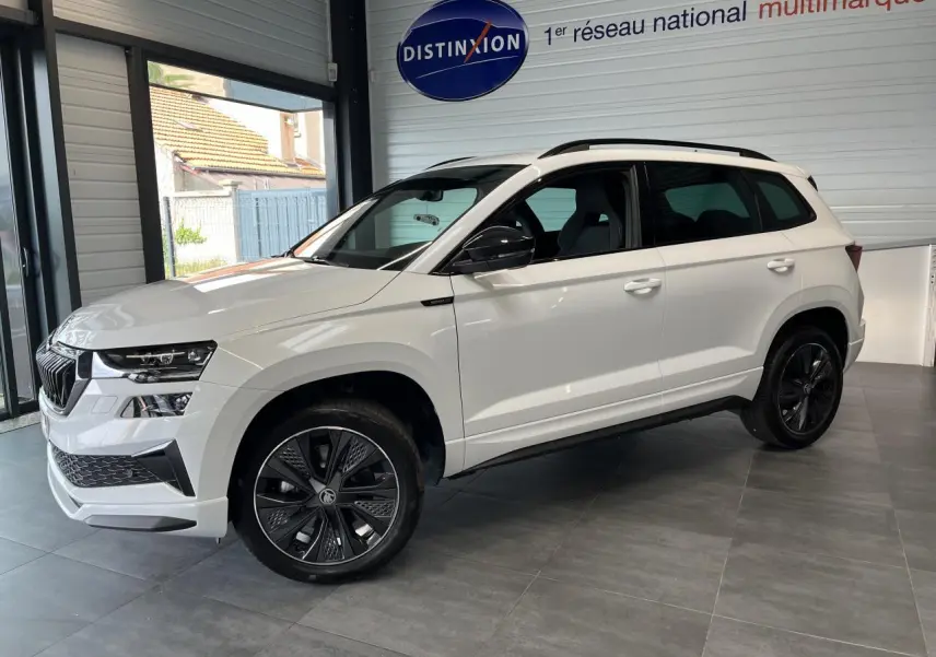 Vue 3/4 avant droite d'un SUV Skoda Karoq blanc avec jantes noires et rétroviseurs noirs dans un showroom.