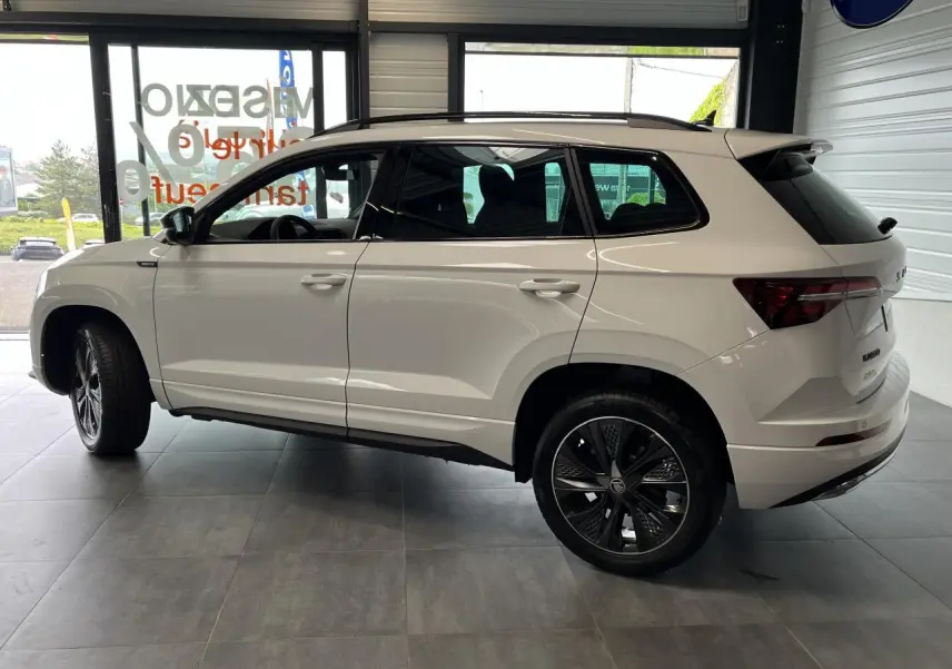 Profil droit du SUV blanc SKODA KAROQ 2025 Sportline avec jantes alliage noires et toit noir brillant.