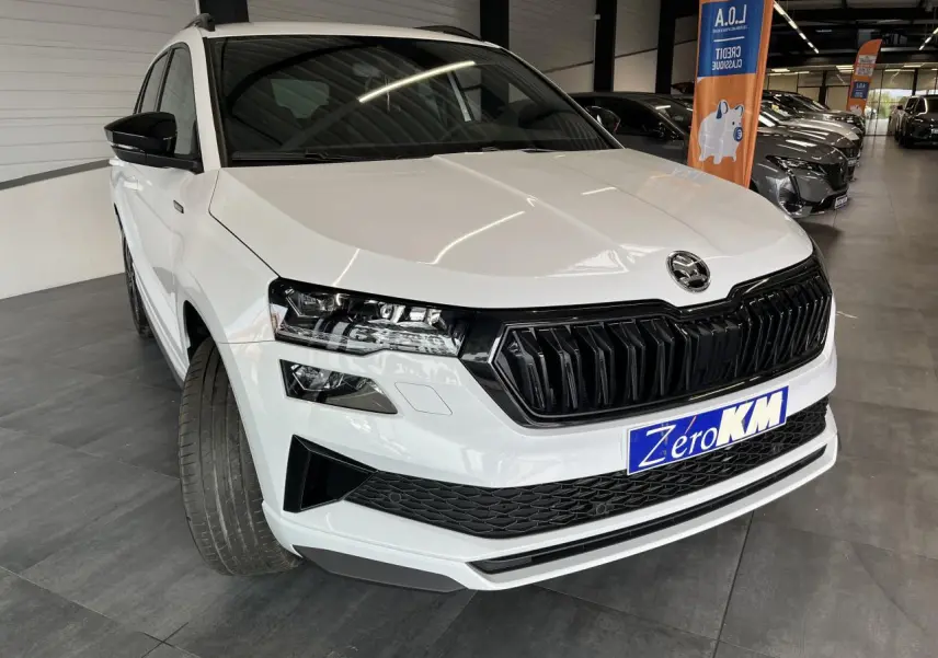 Vue 3/4 avant d'un SUV SKODA KAROQ blanc avec calandre noire et phares LED dans un showroom.