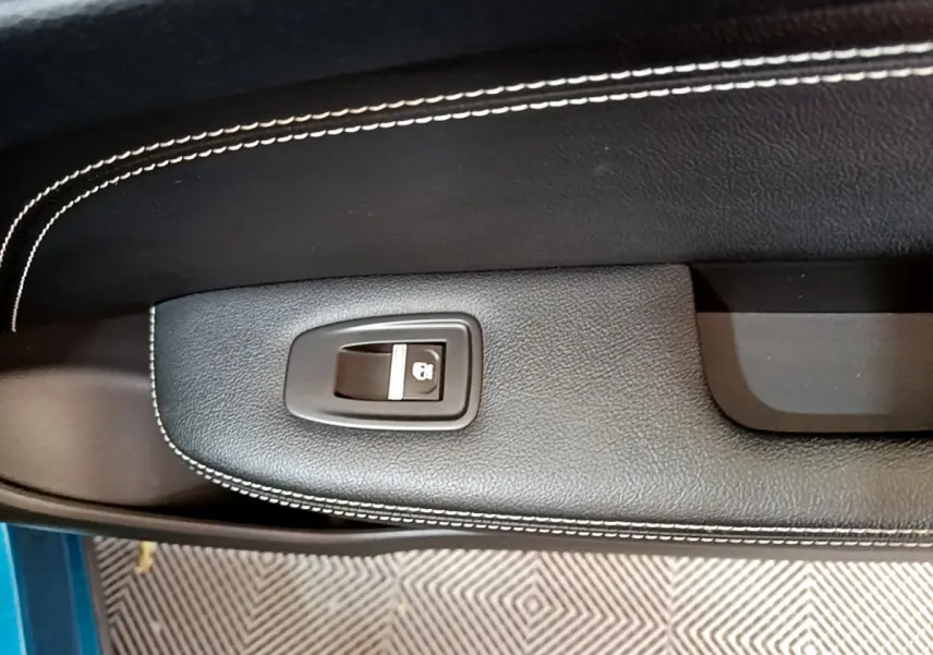 Détail de la commande de verrouillage centralisé sur la portière intérieure noire avec surpiqûres blanches du Renault Arkana bleu.