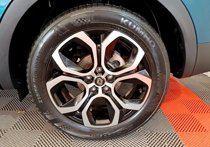 Gros plan sur la roue avant droite du Renault Arkana bleu, jante alliage noire et argent avec logo Renault central.