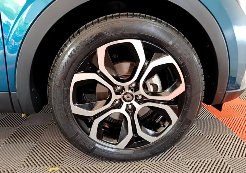 Gros plan sur la roue avant gauche bleu métallisé d'une Renault Arkana Techno E-Tech hybride avec jante alliage noire et argent.