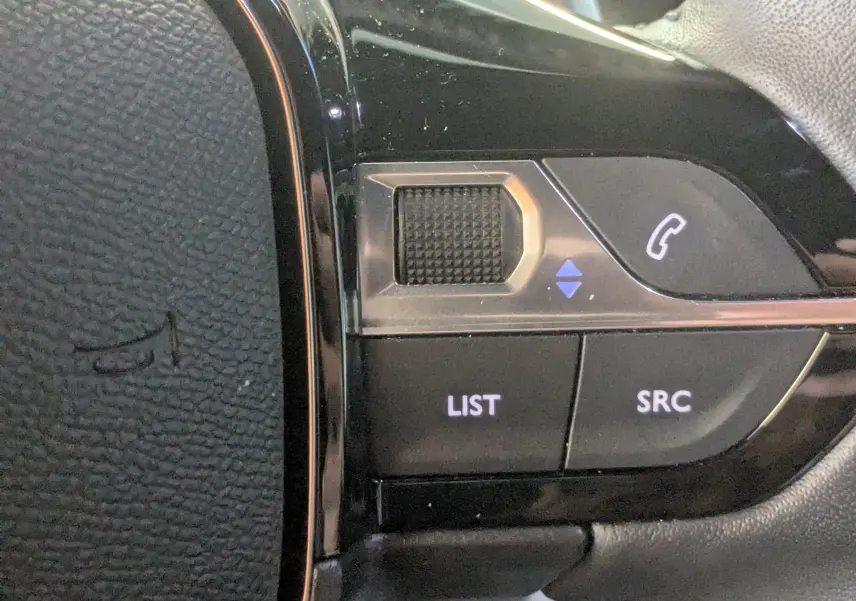 Gros plan sur les commandes du volant noir du Peugeot 2008 130ch eat8 allure, boutons LIST, SRC et téléphone visibles.