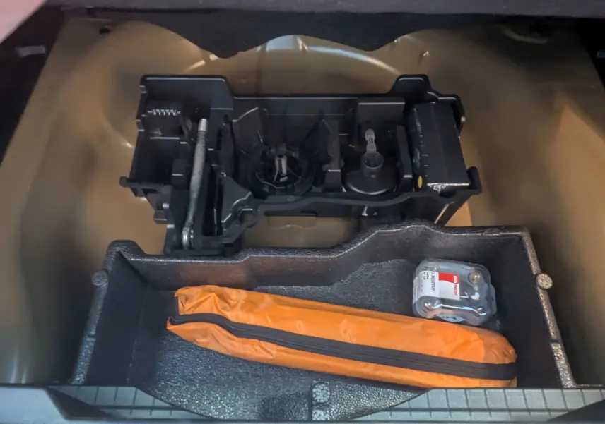 Vue du coffre ouvert d'une Peugeot 2008 noire 2024, montrant le rangement sous plancher avec trousse orange et outils.