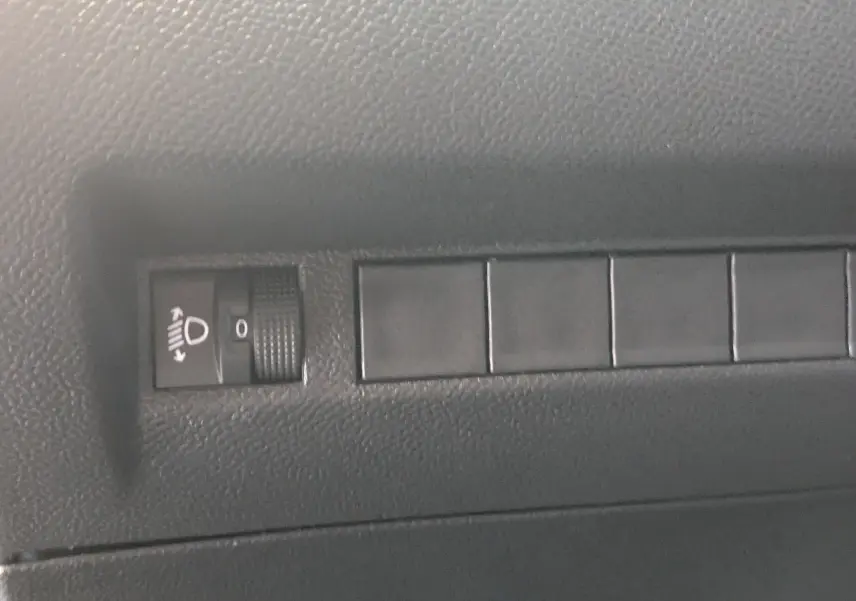 Gros plan sur le réglage de hauteur des phares dans l'habitacle noir du Peugeot 2008 130ch eat8 allure 2024.