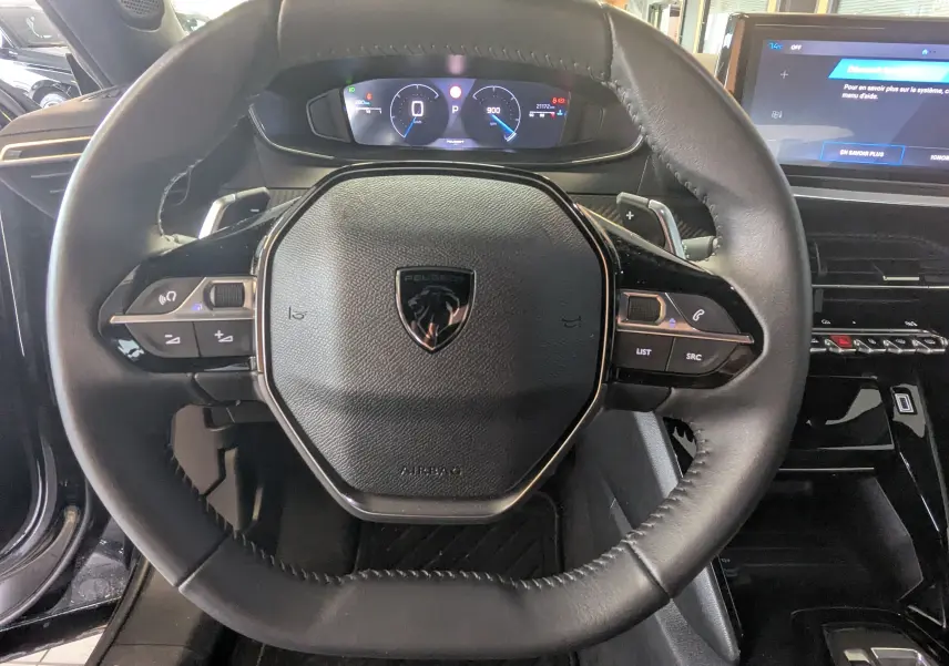 Vue rapprochée du volant cuir noir avec logo Peugeot et tableau de bord numérique du Peugeot 2008 2024.