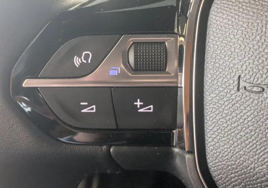 Gros plan sur les commandes de volume et de reconnaissance vocale sur le volant noir du Peugeot 2008 130ch eat8 allure 2024.