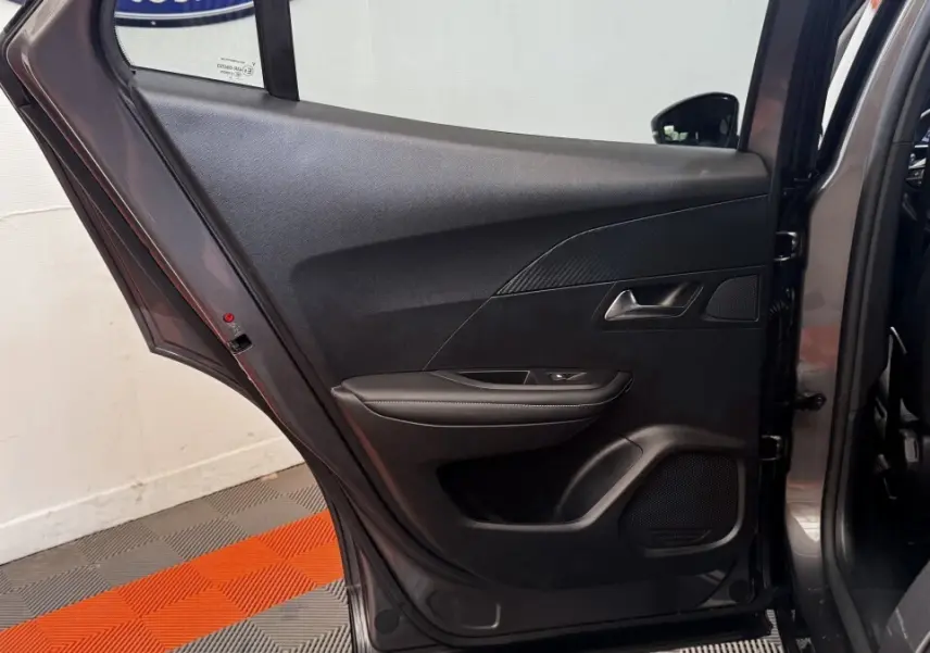 Vue intérieure côté gauche de la porte arrière ouverte d’un Peugeot 2008 gris foncé, avec garniture noire et commande de vitre.