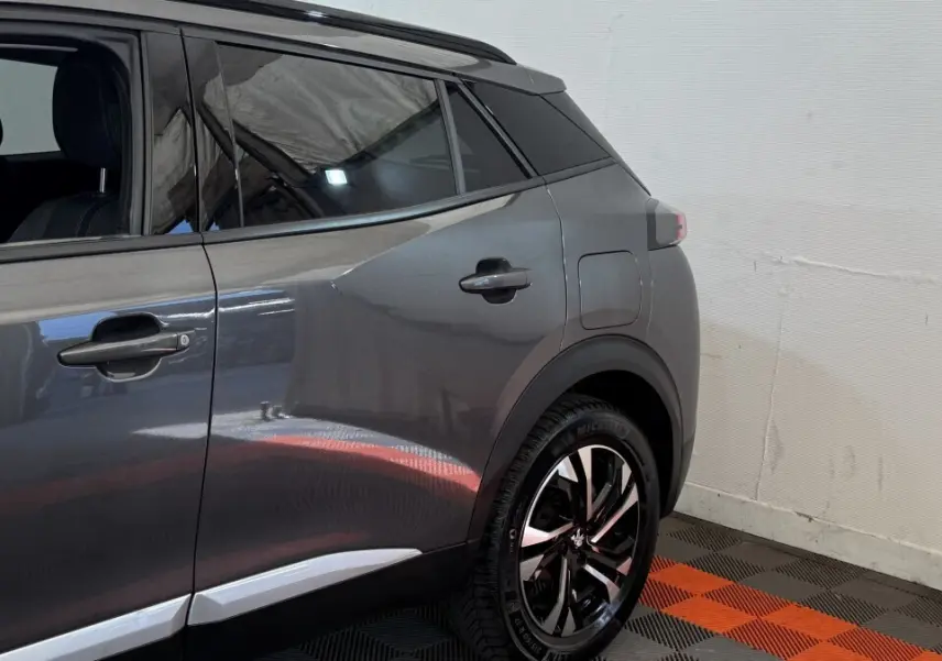 Vue latérale arrière droite d’un Peugeot 2008 gris foncé avec jantes noires et détails chromés sur les portes.