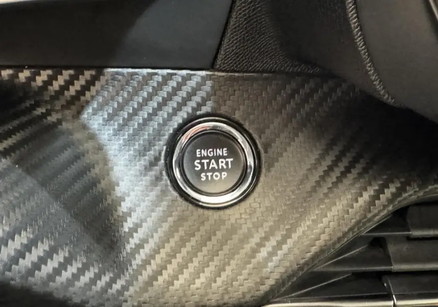 Gros plan sur le bouton start/stop moteur entouré d’un habillage carbone à l’intérieur du Peugeot 2008 gris foncé.