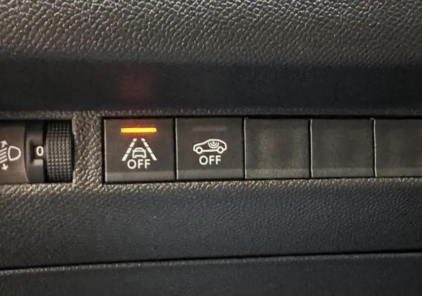 Gros plan sur les boutons de commande du tableau de bord du Peugeot 2008 gris foncé, avec témoin orange allumé.