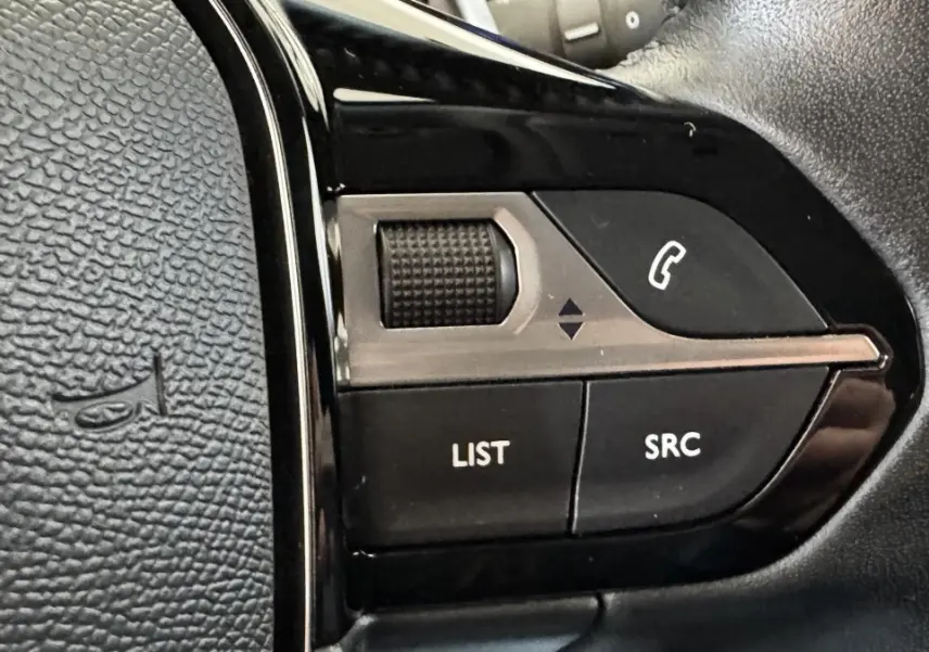 Gros plan sur les commandes multifonctions noires du volant cuir d’un Peugeot 2008 gris foncé, version 2022.