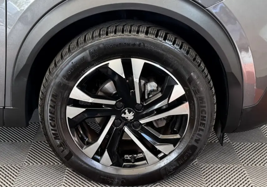 Gros plan sur la roue avant droite d’un Peugeot 2008 gris foncé, avec jante alliage noire et argentée au design moderne.