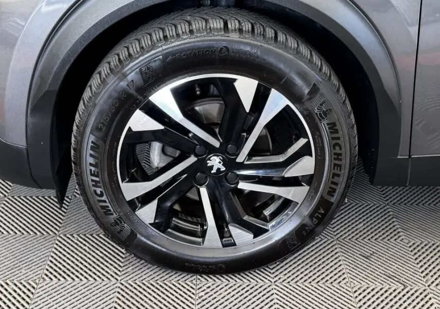 Gros plan sur la roue avant droite du Peugeot 2008 gris foncé, jante alliage noire et argent avec logo lion central.