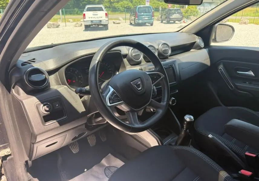 Vue intérieure côté conducteur du Dacia Duster gris 2021, montrant le volant, tableau de bord et levier de vitesses manuel.