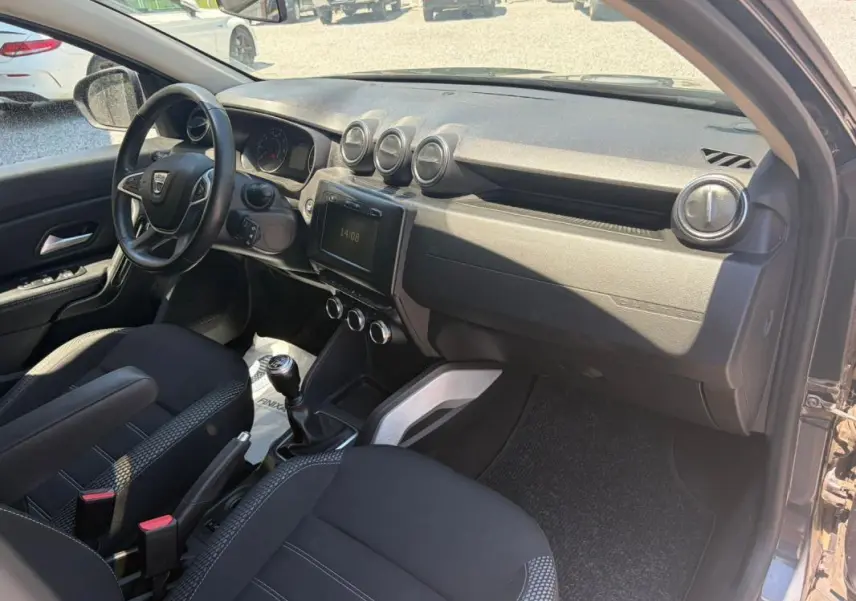 Vue intérieure côté conducteur du Dacia Duster gris 2021, mettant en valeur le tableau de bord et la boîte manuelle.