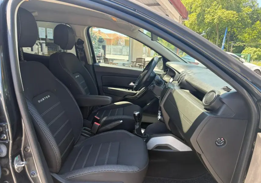 Vue intérieure côté conducteur du Dacia Duster gris 2021, sièges noirs avec logo Duster et levier de vitesses manuel visible.