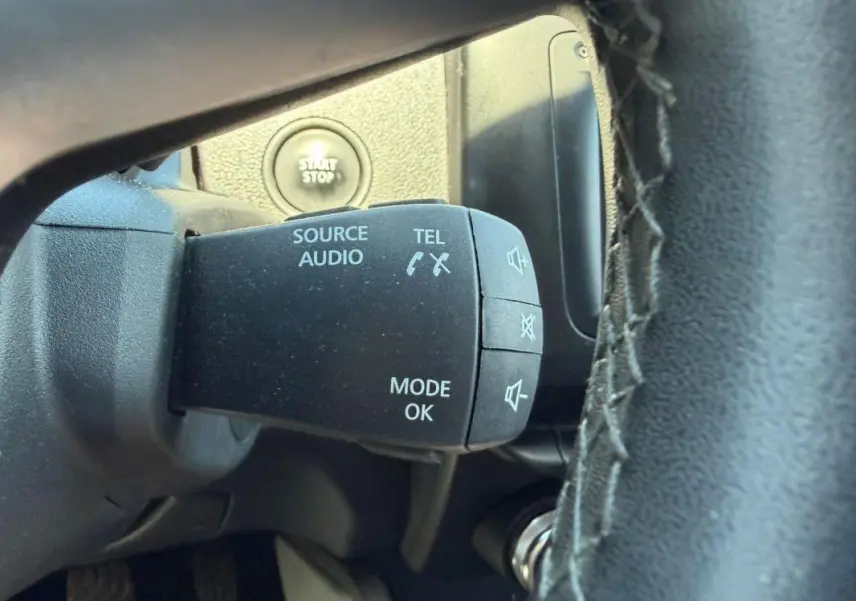 Gros plan sur la commande audio au volant du Dacia Duster gris, avec bouton start/stop visible en arrière-plan.