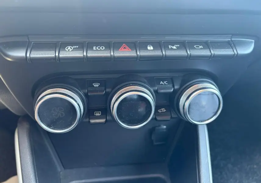 Tableau de bord du Dacia Duster 2021, vue rapprochée des commandes de climatisation et des boutons fonctionnels noirs.
