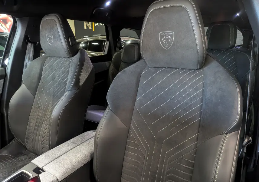 Gros plan sur les sièges avant en cuir noir et alcantara avec logo Peugeot embossé, intérieur du 5008 Hybrid 2025.