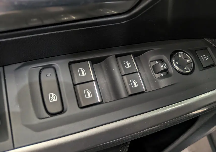 Gros plan sur les commandes de lève-vitres et réglage des rétroviseurs côté conducteur du Peugeot 5008 Hybrid 2025 noir Perla.