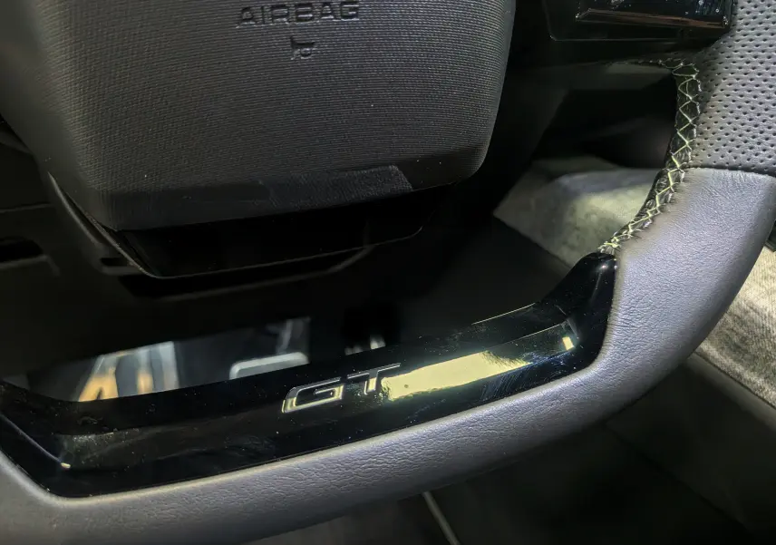 Gros plan sur le volant noir perforé du Peugeot 5008 HYBRID 145 CH e-DCS6 GT avec logo GT en bas.