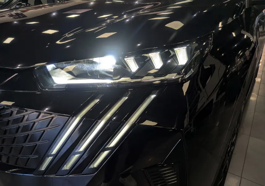 Gros plan sur le phare avant droit allumé du Peugeot 5008 Hybrid noir Perla, soulignant les LED distinctives en griffes.