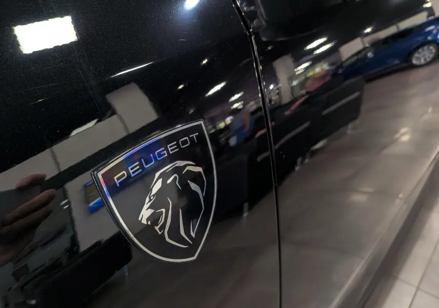 Gros plan sur l'écusson Peugeot noir brillant sur la porte latérale gauche d'un 5008 HYBRID 145 CH e-DCS6 GT Noir Perla.