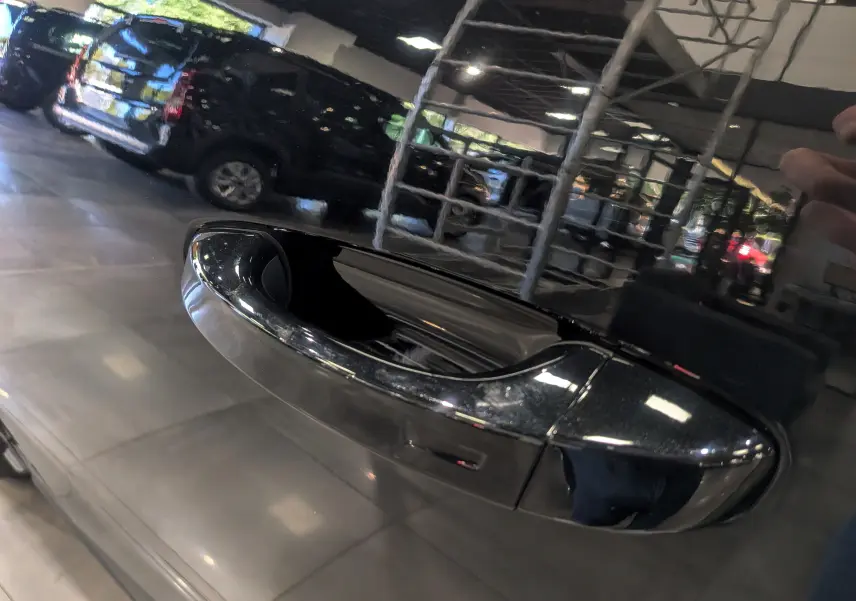 Poignée de porte noire brillante du Peugeot 5008 HYBRID 145 CH e-DCS6 GT 2025, reflet d'un parking intérieur.