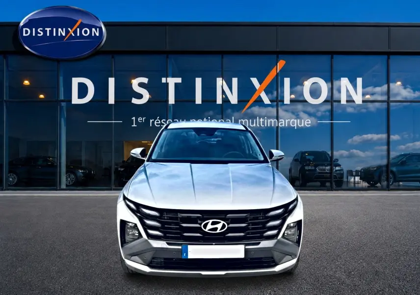 Vue frontale d'un Hyundai Tucson blanc 2026 hybride devant une vitrine avec logo Distinxion.