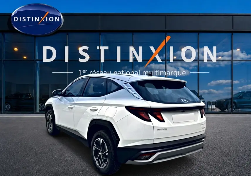 Vue 3/4 arrière droite du Hyundai Tucson blanc hybride 2026 avec jantes alliage et feux arrière LED, devant un showroom Distinxion.