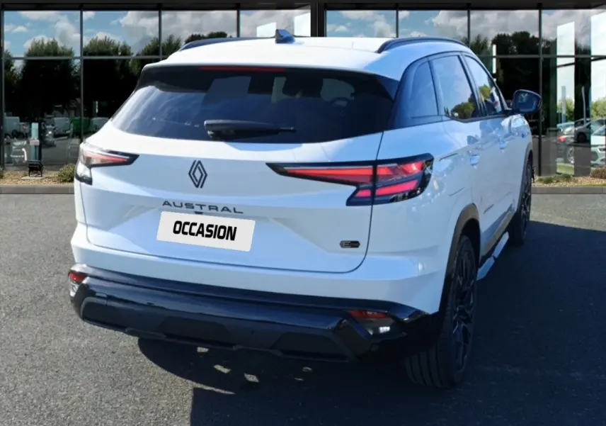 Vue 3/4 arrière droite d'un Renault Austral blanc avec feux arrière LED et logo central sur fond urbain.