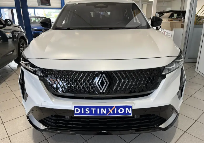 Vue frontale du Renault Rafale blanc avec calandre noire à motif 3D et logo central brillant dans un showroom.