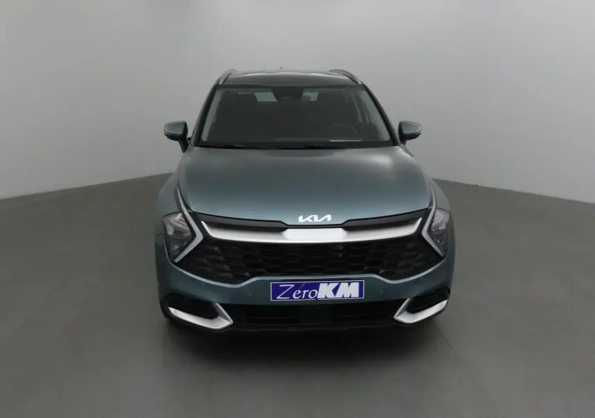 Vue frontale d'un KIA Sportage gris Sirius 2025 avec calandre noire et logo KIA lumineux sur capot.